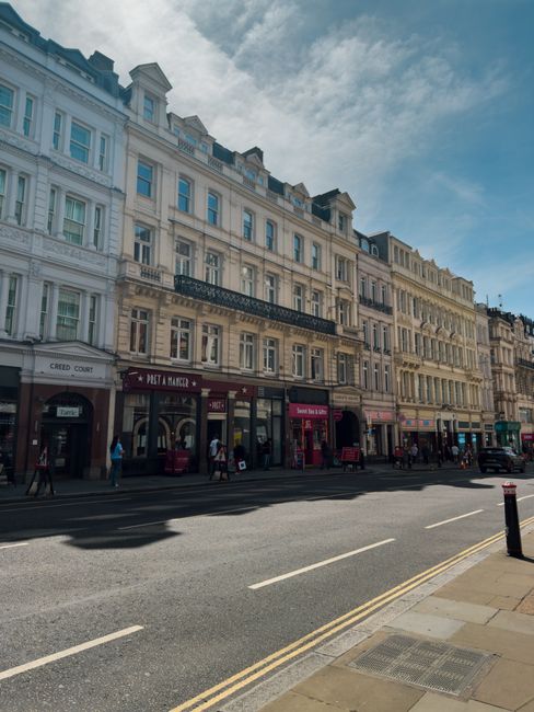 A wide view of a residential street in Earls Court, SW5, with elegant white Victorian-style buildings featuring ornate facades, large windows, and balconies. The street is lined with parked cars and l