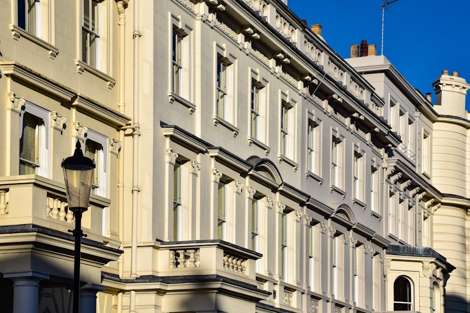 Close-up view of the exterior façade of a multi-storey residential building in Earls Court, featuring cream-colored stone walls with decorative moldings and sash windows. The building displays ornate